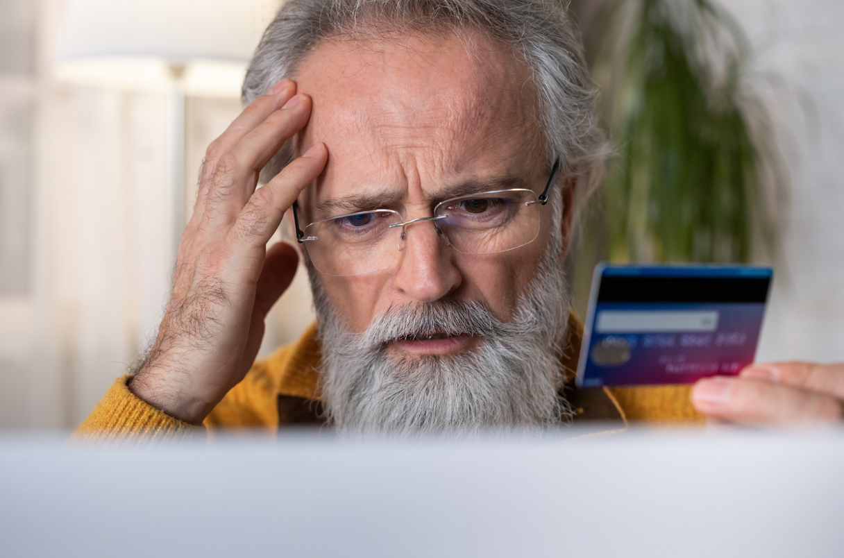 Distressed older man looking at computer screen and holding credit card