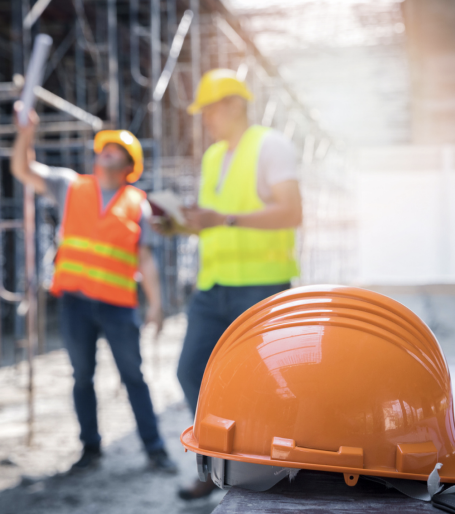 Construction hard hat, with two conversing construction workers in the background on site.