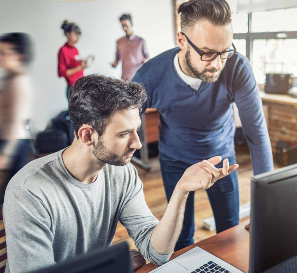 Two casually-dressed office colleagues discussing content on a computer screen